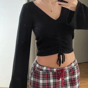 Svart croppad topp med v-ringning och knyt - Säljer en svart croppad topp med lång ärm och v-ringning. Toppen har knytning framtill som ger en snygg rynkad effekt. Perfekt till jeans eller kjol för en trendig look.