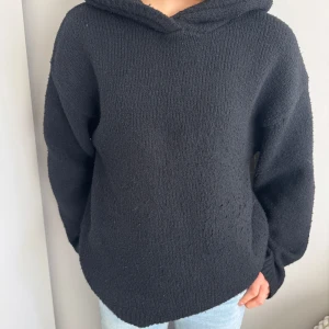 Svart stickad hoodie - Mysig svart stickad hoodie med lång ärm och avslappnad passform. Perfekt för kyliga dagar och enkel att matcha med jeans eller leggings. Klassisk huva och mjukt material.