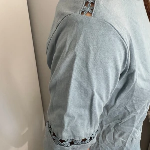 Ljusblå topp med spetsdetaljer - Säljer en ljusblå topp med korta ärmar och fina spetsdetaljer vid axlar och ärmslut. Perfekt för dig som gillar enkla men snygga detaljer. Toppens material känns mjukt och bekvämt.