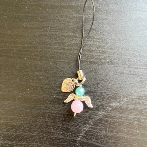 Rosa och blå lycko ängel 🩵 - Sött mobilhänge med en ängel gjord av en rosa och en turkos pärla samt silvriga vingar. Hängsmycket har även en liten hjärtberlock med texten 'made with love'. Perfekt som accessoar till mobilen eller väskan.🩵