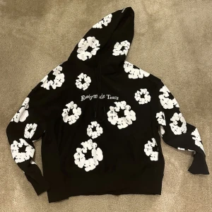 Svart denim tear hoodie ready ro wear  - Säljer en svart hoodie från Readymade med stora vita blommönster över hela tröjan och texten 'Readymade Tears' på bröstet. Tröjan har huva och långa ärmar, perfekt för en cool och avslappnad stil.