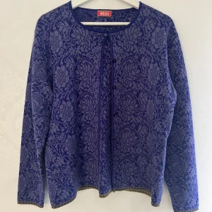 Lila mönstrad kofta från Oleana - Superfin lila kofta från Oleana med vackert blommigt mönster i ljuslila och dekorativa kanter. Koftan har rund halsringning, knappar framtill och långa ärmar. Original pris 1000 kronor