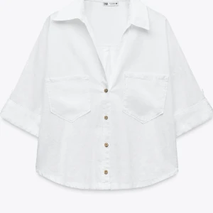 Vit croppad linneskjorta med fickor från Zara - Säljer en vit croppad linneskjorta från Zara med två stora bröstfickor och knappar framtill. Skjortan har en avslappnad passform och luftig känsla. Aldrig använts 