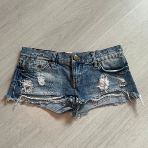 Blå jeansshorts med slitningar - Skitsnygga lågmidjade jeansshorts från river Island!! Midjemåttet är 38cm🥰
