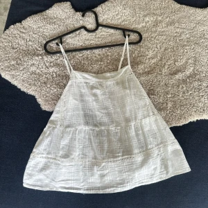 Vit linnetopp - Säljer en söt vit linnetopp från Gina Tricot med tunna axelband och fina spetsdetaljer. Toppen har knytning i ryggen och ett luftigt, lätt material som passar perfekt till varma dagar.