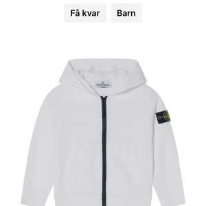 Vit hoodie från Stone Island - Vit hoodie från Stone Island med dragkedja och klassisk logotyp-patch på ärmen. Tröjan har huva och fickor framtill, samt svarta detaljer vid dragkedjan. Perfekt för en stilren och sportig look.