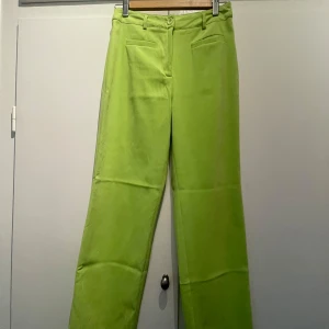 Limegröna kostymbyxor - Säljer ett par limegröna kostymbyxor med raka ben och hög midja. Byxorna har två fickor fram och stängs med knapp och dragkedja. Det finns en små fläck på byxorna - se bild. 