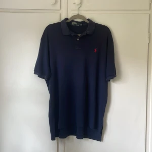 Mörkblå pikétröja från Polo Ralph Lauren - Klassisk och tidlös pikétröja i mörkblått från Polo by Ralph Lauren. Ikoniska röda loggan på bröstet och en bekväm passform. Perfekt till både vardags och mer uppklädda tillfällen! Använd men i fint skick, inga hål eller fläckar.  Nypris: ca 1 200 kr, Mitt pris: 349 SEK