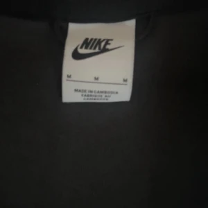Svart Nike hoodie med dragkedja - Säljer en svart Nike hoodie med dragkedja och huva. Jackan har en gul Nike-logga på bröstet och är tillverkad i ett mjukt material. Perfekt för träning eller chill. Klassisk design med lång ärm och fickor framtill.