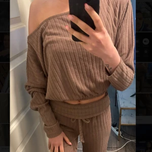 Bruna ribbade mjukisbyxor och matchande tröja -set  - Mysiga bruna mjukisbyxor i ribbat material med resår och dragsko i midjan. Byxorna har en rak och avslappnad passform, perfekta för en chill vardagslook. Kommer med en matchande tröja som är off shoulder på ena sidan. Tight passform 
