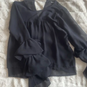 Svart blus från bikbok - Sen svart blus från bikbok med volanger på en större del av underarmen. Den är i mesh material🫶🏽😌