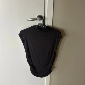 Svart ärmlös topp - En enkel svart ärmlös topp i mjukt material. Topp har en rak passform och är perfekt för en stilren look. Passar bra till varma dagar eller som basplagg att styla med accessoarer.