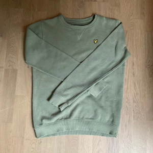 Grön sweatshirt från Lyle & Scott - Säljer en stilren grön sweatshirt från Lyle & Scott Junior med klassisk gul broderad logga på bröstet. Tröjan har rund halsringning, långa ärmar och ribbade muddar vid ärmslut och nederkant. Perfekt för en avslappnad look.