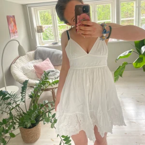 Vit somrig klänning med broderade detaljer - Söt vit klänning med v-ringning och smala axelband. Klänningen har broderade detaljer nertill och en luftig, lätt kjol. Perfekt för sommaren!!!