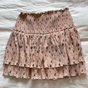 Blommig volangkjol från NA-KD - Supersöt ljusrosa kortkjol från NA-KD med små blommor och volangdetaljer. Kjolen har smock i midjan för en bekväm passform och dubbla lager tyg som ger en fin volym. Perfekt för vår och sommar! Tyvärr är kjolen för stor för mig så kan ej skicka bilder med den på! 