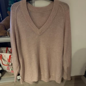 Ljusrosa ribbad stickad tröja från Lindex - Mysig ljusrosa stickad tröja från Lindex med djup v-ringning och ribbad struktur. Tröjan har lång ärm och en avslappnad passform, perfekt för lager-på-lager under kyliga dagar.