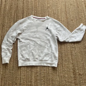 Vit camomönstrad sweatshirt från Jordan - Säljer en vit sweatshirt från Jordan med diskret camomönster och klassisk Jumpman-logga på bröstet. Tröjan har rund halsringning och långa ärmar. Perfekt för en sportig och avslappnad stil.