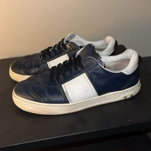 Valentino sneakers i blått och vitt - Säljer ett par snygga Valentino sneakers i mörkblått skinn med vita detaljer och vit sula. Skorna har svart snörning och en klassisk rund tå. Perfekta för dig som gillar stilrena och exklusiva sneakers. Skorna säljs ej i butik längre, de har haft en ägare innan mig och jag säljer dom då dom blivit för små. Skriv för fler bilder eller om du har någon fundering!😊