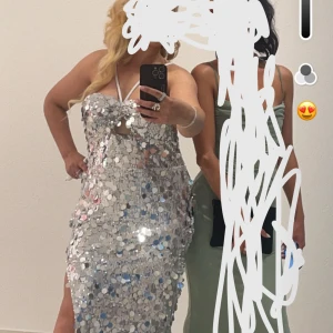 Glittrig silver långklänning med paljetter - Säljer en glittrig långklänning i silver med stora paljetter och slits framtill. Klänningen har smala axelband och en figurnära passform som framhäver siluetten. Perfekt för dig som vill sticka ut på festen!