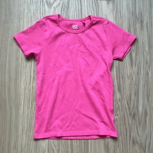Rosa t-shirt från 157 - En enkel och snygg rosa t-shirt från 157. T-shirten har rund halsringning och korta ärmar. Perfekt till sommaren och lätt att matcha med jeans eller shorts. Lappen kvar, helt ny, aldrig använd.