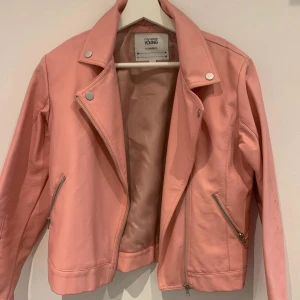 Ljusrosa skinnjacka  - Säljer en ljusrosa skinnjacka med klassisk bikerstil. Jackan har silvriga dragkedjor, snedställd dragkedja framtill och tryckknappar vid kragen. Perfekt för att lyfta vilken outfit som helst.
