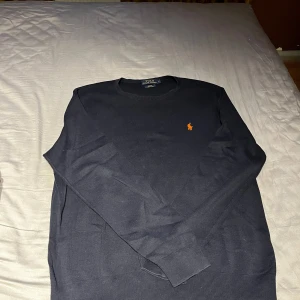 Mörkblå tröja från Polo Ralph Lauren - Säljer en mörkblå tröja från Polo Ralph Lauren i slim fit-modell. Tröjan är i mjuk bomull och har en klassisk rund halsringning samt den ikoniska broderade loggan i orange på bröstet. Storlek L men passar även storlek M. Öppen för prisförslag!