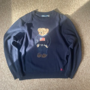 Mörkblå stickad tröja Polo bear tröja - Mörkblå stickad tröja från Polo Ralph Lauren med klassisk björn på bröstet och broderade RL-initialer nertill. Tröjan har rund halsringning och ribbade muddar vid ärmslut och nederkant. Perfekt för dig som gillar preppy stil. Skicka 8.5/10 köpt secondhand men använt sparsamt. Priset är som alltid diskuterbart, skriv för fler frågor mina vänner❤️‍🔥🍾