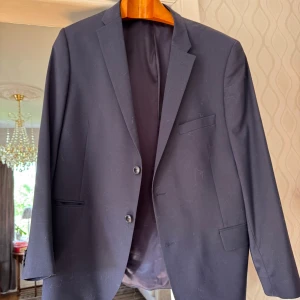 Mörkblå kavaj från Turo - Stilren mörkblå kavaj från Turo med modern fit. Kavajen har två knappar framtill, klassiska fickor och en bröstficka. Fodret är ljusblått med en innerficka. Perfekt för dig som vill ha en tidlös och snygg look. köparen står för frakten! Nypris 2500kr säljs för 300kr då han som ägde den avled hastigt! Matchande byxor finns att köpa separat 