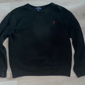 Svart sweatshirt från Polo Ralph Lauren - Klassisk svart sweatshirt från Polo Ralph Lauren med rund halsringning och röd broderad logga på bröstet. Tröjan har långa ärmar och är tillverkad i mjuk bomull, perfekt för en avslappnad stil. Skriv vid frågor, pris kan diskuteras. XS-S