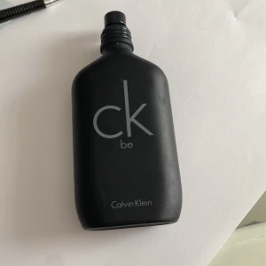 CK Be Eau de Toilette från Calvin Klein - En stilren svart parfymflaska från Calvin Klein med texten 'ck be' i grått. Flaskan har en matt finish och minimalistisk design, perfekt för dig som gillar klassiska och fräscha dofter. Mer än halva flaskan är fylld