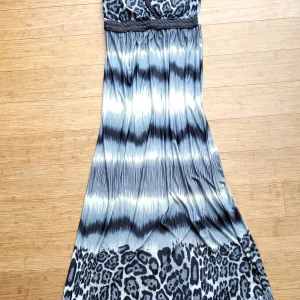 Långklänning med leopardmönster - Säljer en snygg långklänning med svart, grått och vitt leopardmönster. Klänningen har flätade axelband, omlott-v-ringning och ett brett flätat band under bysten. Materialet är mjukt o strechigt men tungt så snyggt fall I tyget. Anv 3 ggr bara.