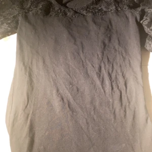 Svart t shirt med spets från Sisters - Svart t shirt från Sisters i storlek XS. Klänningen har fina spetsdetaljer upptill och korta ärmar. Perfekt för dig som gillar en klassisk och stilren look.