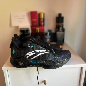 Kyrie Anta - Säljer ett par svarta sneakers med unika färgglada mönster och detaljer i blått, gult, orange och vitt. Skorna har snörning, rund tå och platt sula. Materialet är en mix av syntet och mesh för bra andningsförmåga. Perfekta för dig som vill sticka ut med din stil.