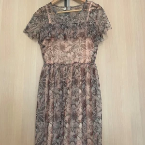 Blommig meshklänning från Rainbow - Säljer en söt blommig klänning från Rainbow i meshmaterial. Klänningen har korta ärmar, volangdetalj vid bysten och ett skirt lager över en ljusrosa underklänning. Perfekt för dig som gillar fina mönster. Endast prövad💕