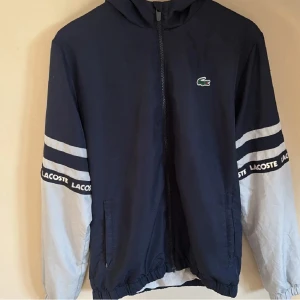Lacoste vind jacka  - Säljer då jag ej använder, jackan är i rätt nytt skick men den har en fläck på ena armen som ni kan se på en av bilderna där av priset