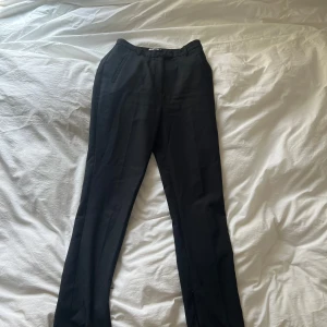 Svarta kostymbyxor från NA-KD - Säljer ett par svarta kostymbyxor från NA-KD med klassisk passform och raka ben. Byxorna har diskreta fickor i sidorna och stängs med dragkedja och knapp. Perfekta till en stilren look.