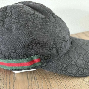 Svart keps från Gucci  - Svart keps från Gucci med klassiskt GG-monogram över hela ytan och grönt/rött band på sidan. Kepsen är i perfekt skick.                                OBS! Pris kan diskuteras