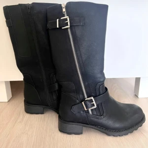 Svarta stövlar med dragkedja och spänne - Säljer ett par svarta stövlar med grov sula, dekorativa spännen och dragkedja på sidan. Stövlarna har rund tå och är perfekta för höst och vinter. Snyggt och stilrent val till många outfits. Fodrade invändigt