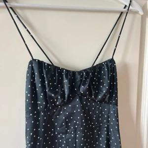 Svart långklänning smala axelband - Säljer en svart långklänning med vita prickar och smala axelband. Klänningen har omlottknytning i ryggen och är ärmlös. Perfekt för sommaren.