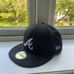 Svart keps från New Era 59FIFTY Atlanta Braves - Säljer en svart New Era 59FIFTY keps med Atlanta Braves-logga broderad framtill i vitt. Klassisk modell med platt skärm och broderad MLB-logga bak. Perfekt för dig som gillar sportig stil.