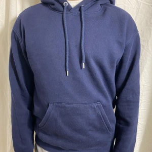 Mörkblå hoodie med magficka - Säljer en enkel och stilren mörkblå hoodie med huva och dragsnören. Tröjan har en stor magficka framtill och är tillverkad i mjukt material. Perfekt för en avslappnad look.