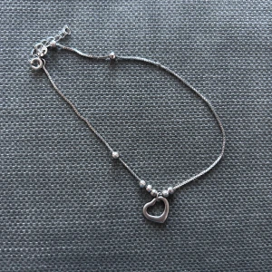Silver fotlänk  med hjärthänge - Säljer ett tunt och stilrent fotlänk  i silver 925 med små kulor och ett öppet hjärthänge. Perfekt för dig som gillar enkla smycken med en söt detalj. Justerbar längd med kedja och lås.