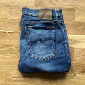 Nudie Jeans - Säljer ett par klassiska blå jeans från Nudie Jeans med normal passform och raka ben. Byxorna har fem fickor, synliga sömmar och en snygg tvättad look. Perfekta för dig som gillar stilrena och tidlösa jeans. (Dam Jeans)