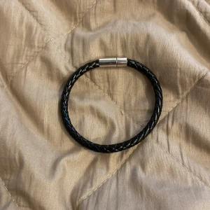 Svart flätat armband av plast  - Snyggt svart armband med flätad design. Perfekt accessoar för att lyfta din outfit med en enkel men modern touch. Passar både till vardags och när du vill känna dig extra snygg.