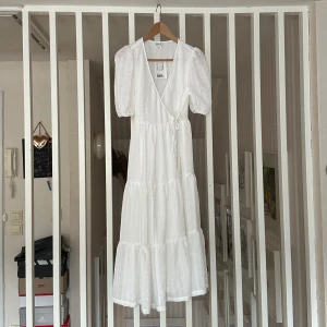 Vit dubbelomlottklänning - Superfin vit långklänning med dubbel omlott. Klänningen har korta puffärmar och volangdetaljer i kjolen. Perfekt för sommarens alla tillfällen och ger en romantisk känsla. Köptes i london för nått år sedan och har aldrig använts