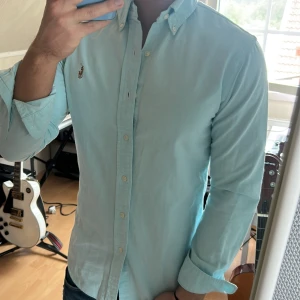 Ljusblå skjorta från Ralph Lauren - Säljer en klassisk ljusblå skjorta från Ralph Lauren med broderad logga på bröstet. Skjortan har knappar hela vägen och button-down krage. Perfekt för dig som gillar stilrena och tidlösa plagg.