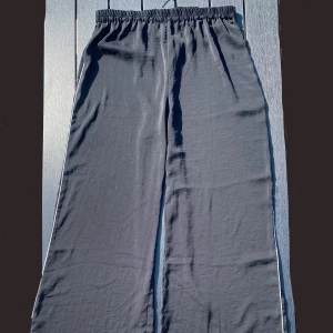 Svarta vida byxor med rak passform - Säljer ett par svarta byxor med rak och lös passform. Byxorna har resår i midjan och en smal silver rand längs sidan av benet. De är lätta och luftiga, passar perfekt till varma dagar nu till sommaren. 