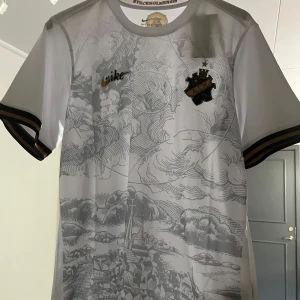 AIK vit fotbollströja med guld- och svartdetaljer från Nike - Säljer en vit AIK fotbollströja från Nike med guld- och svartdetaljer. Tröjan har korta ärmar, AIK:s klubbmärke på bröstet och ett diskret mönster över hela framsidan. Perfekt för dig som vill visa ditt stöd för AIK.