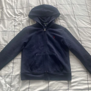 Polo Ralph Lauren Zip-Up Hoodie - Ralph Lauren zip-up hoodie med huva i blå färg För barn som är ca 130 cm långa (7-9 år) 84% bomull och 16% polyester Mjuk och skön insida Bra skick och inga fel på den