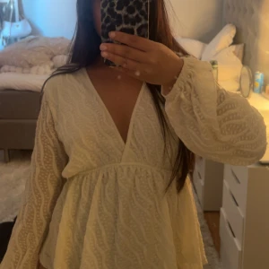 Vit blus med mönster på  - Supersöt vit blus med v-ringning, omlottliv och volang nertill. Långa ärmar med spetsmönster ger en romantisk känsla. Perfekt för sommarens alla tillfällen!